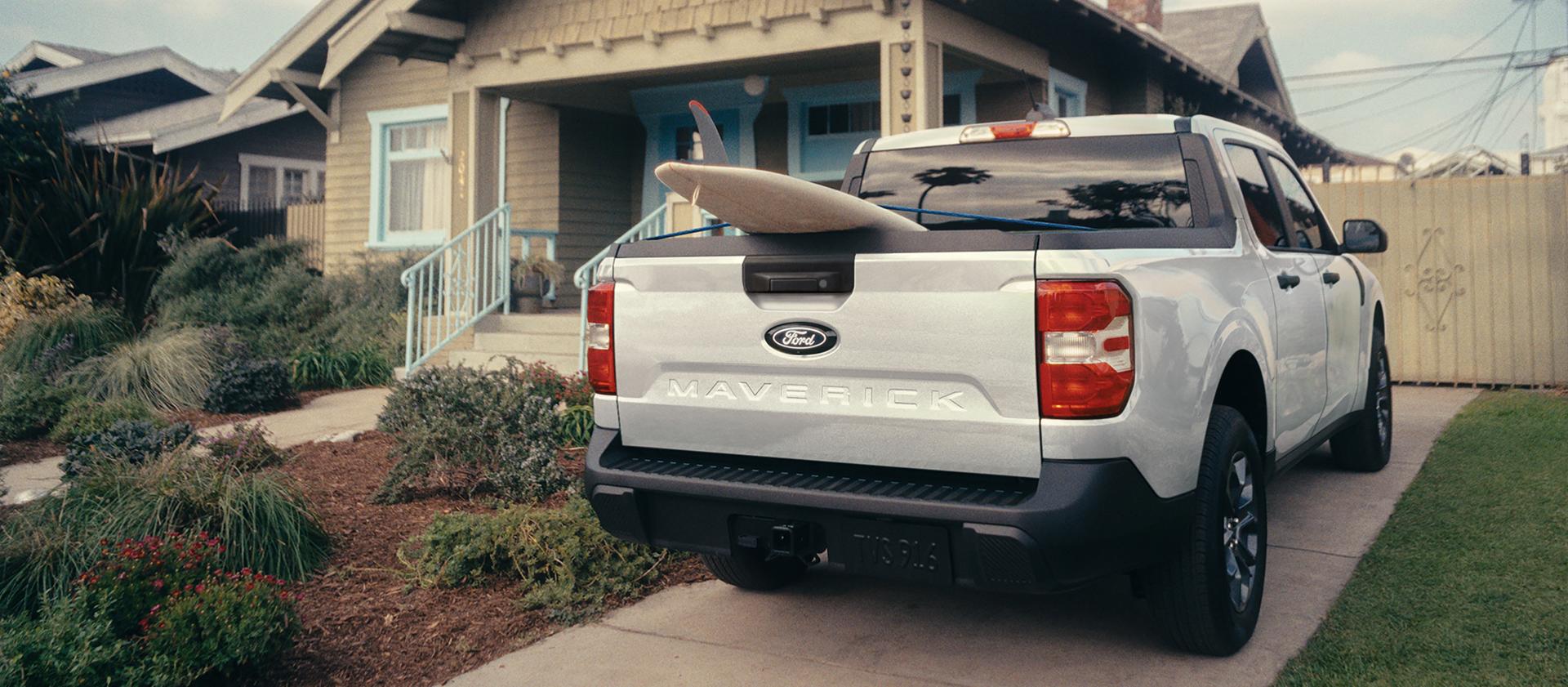 Vue arrière d’un camion Ford Maverick® 2026 avec une planche à rame dépassant du caisson, garée devant une maison