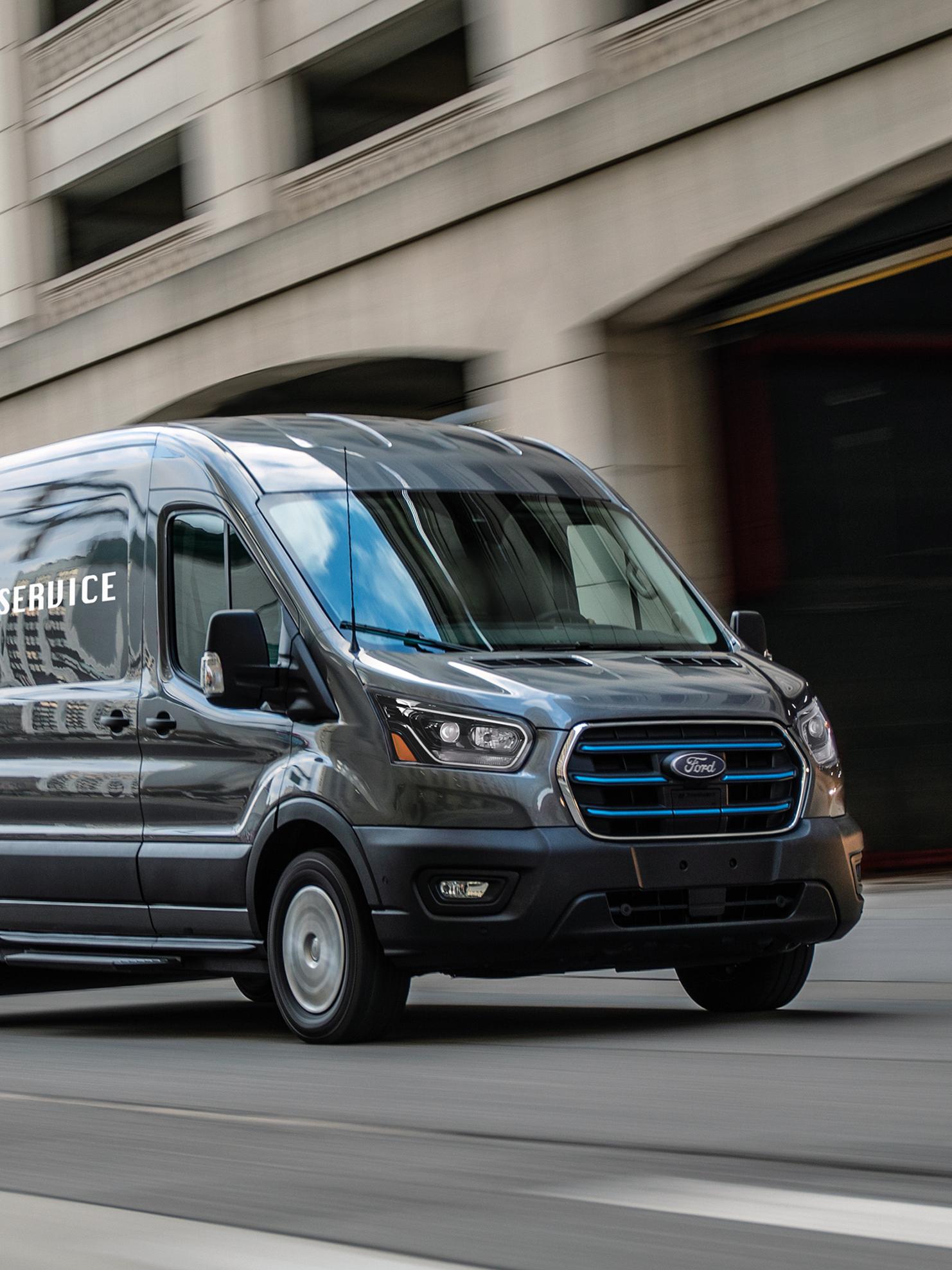 Fourgonnette Ford Transit® 2027 grise roulant en ville, avec un effet de flou de mouvement