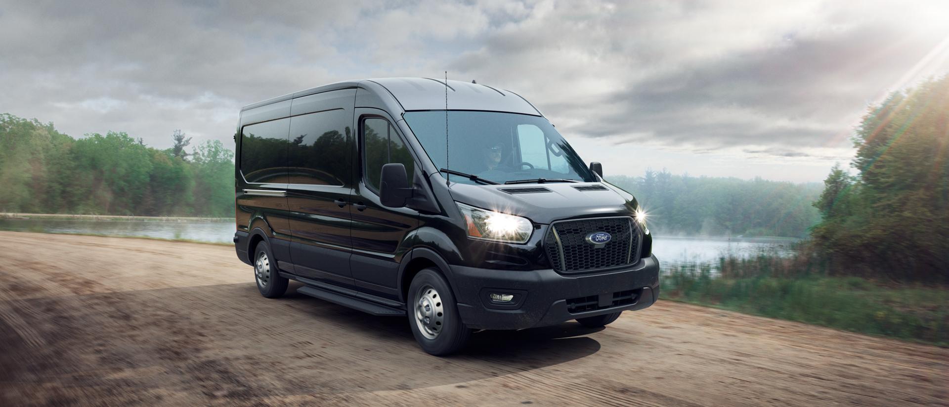 Une fourgonnette Ford Transit® 2025 conduite sur un chemin de terre près d’un plan d’eau