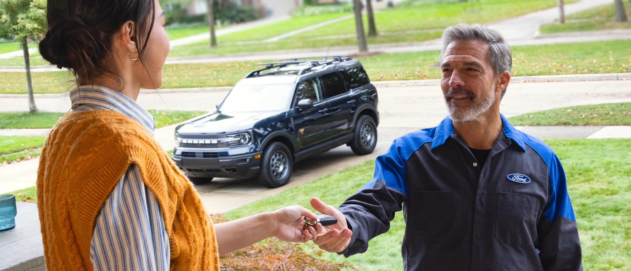 Une propriétaire Ford tend les clés de son Bronco Sport à un technicien de Service Ford venu chercher son véhicule à domicile pour la collecte et livraison.