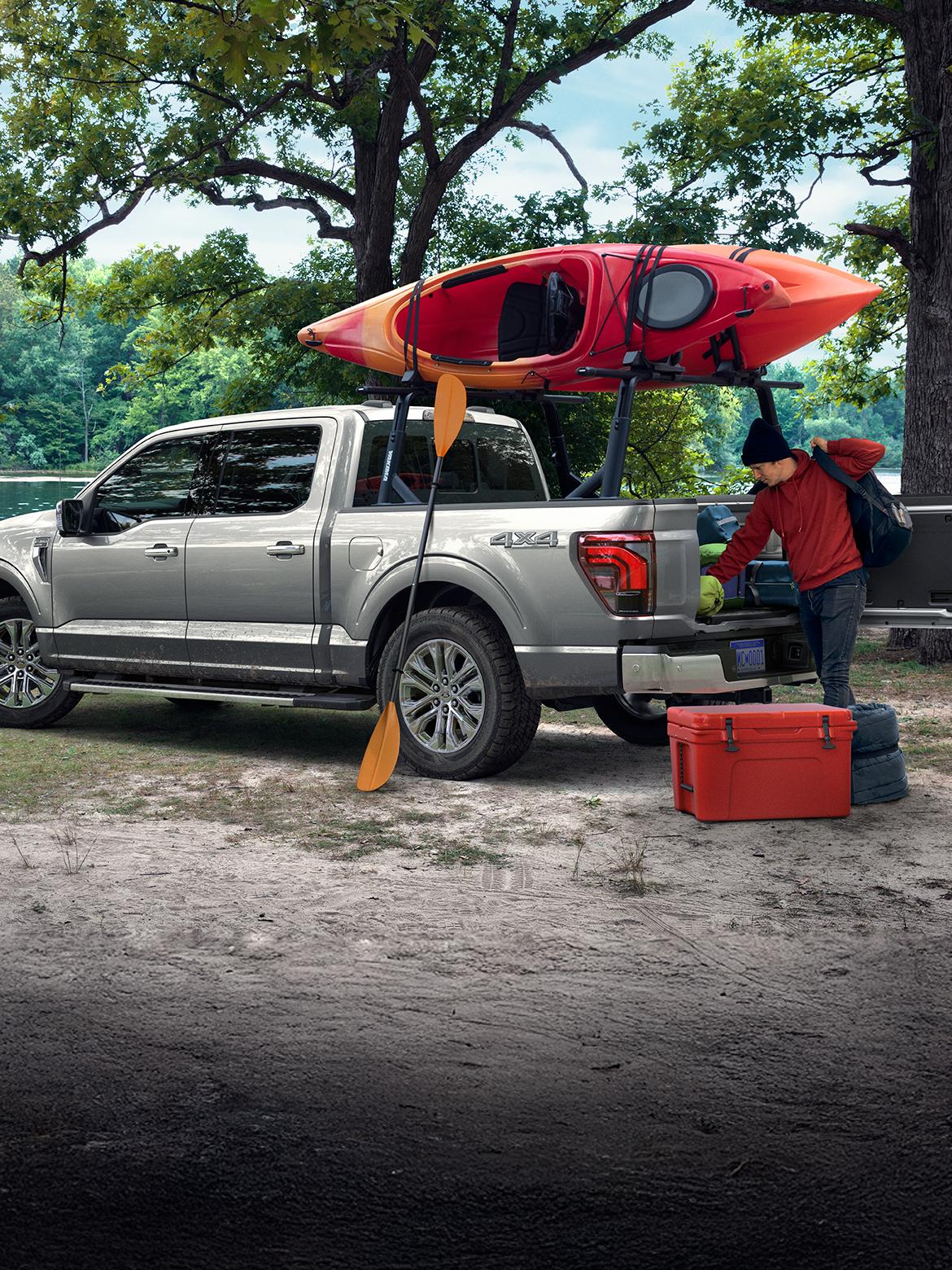 Un F-150 gris avec un canoë fixé sur les barres de toit, stationné près d'un lac.