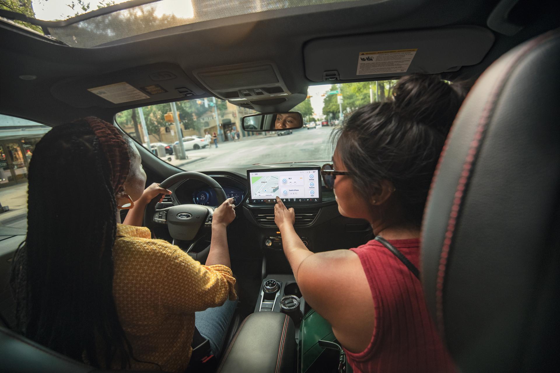 Une femme conduit un véhicule Ford tandis qu'un passager utilise l'écran tactile.
