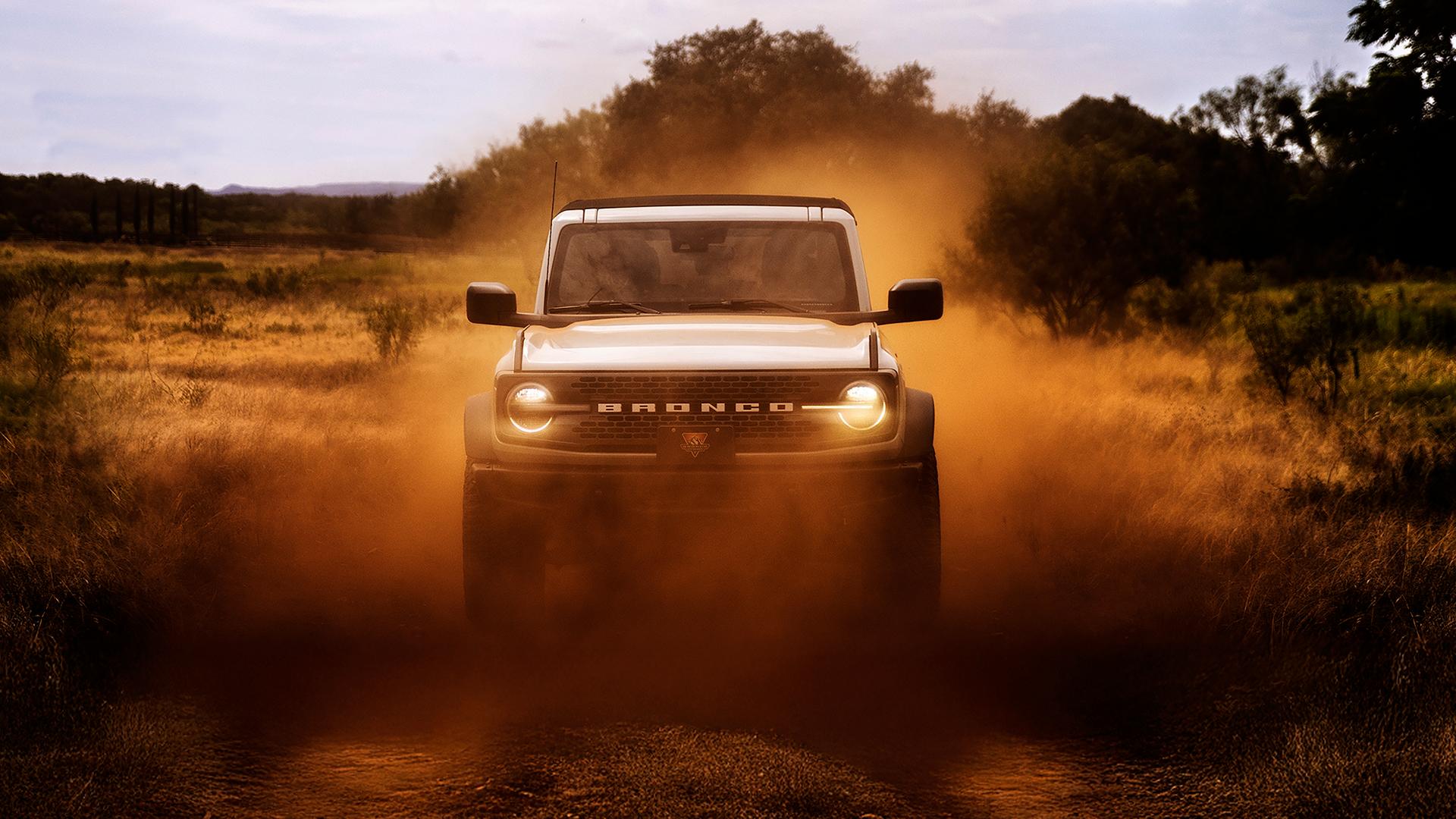 L’avant d’un VUS Ford Bronco® 2026, ses phares brillant à travers un nuage de poussière rouge.