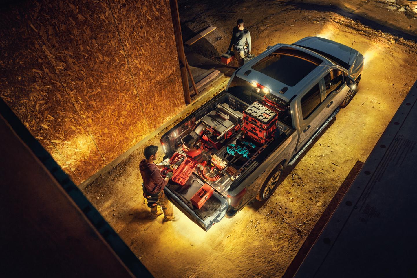 Un F-150 Lightning avec des feux à DEL 360 allumés et une personne qui charge de l'équipement dans la caisse du camion.