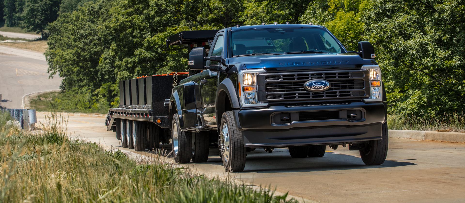 Modèle Ford Super Duty® F-350® Platinum® Plus 2026 en bleu argon tirant une grande remorque à plateau le long d’une colline pavée
