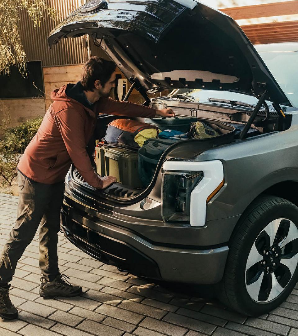 Une personne plonge sa main dans le Mega Power Frunk d’un camion Ford F-150 Lightning® 2025 rempli de boîtes et de sacs