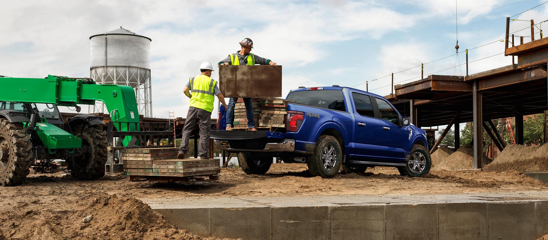 Deux hommes déchargeant des matériaux de construction de la caisse d’une camionnette Ford F-150® STX® FX4 2026 en bleu antimatière métallisé