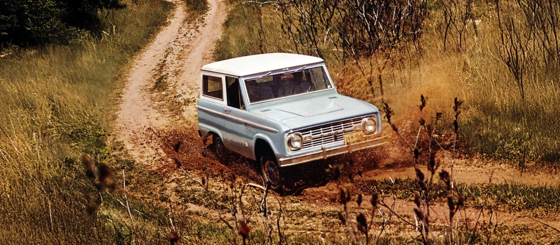 Une fourgonnette Bronco des années 1960 roulant sur un chemin de terre.