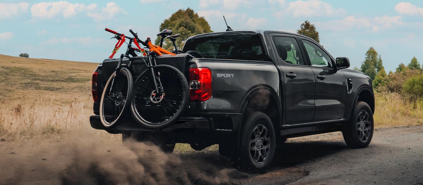 Un camion Ford Ranger® 2026 conduit sur une route de terre avec trois vélos dans la caisse