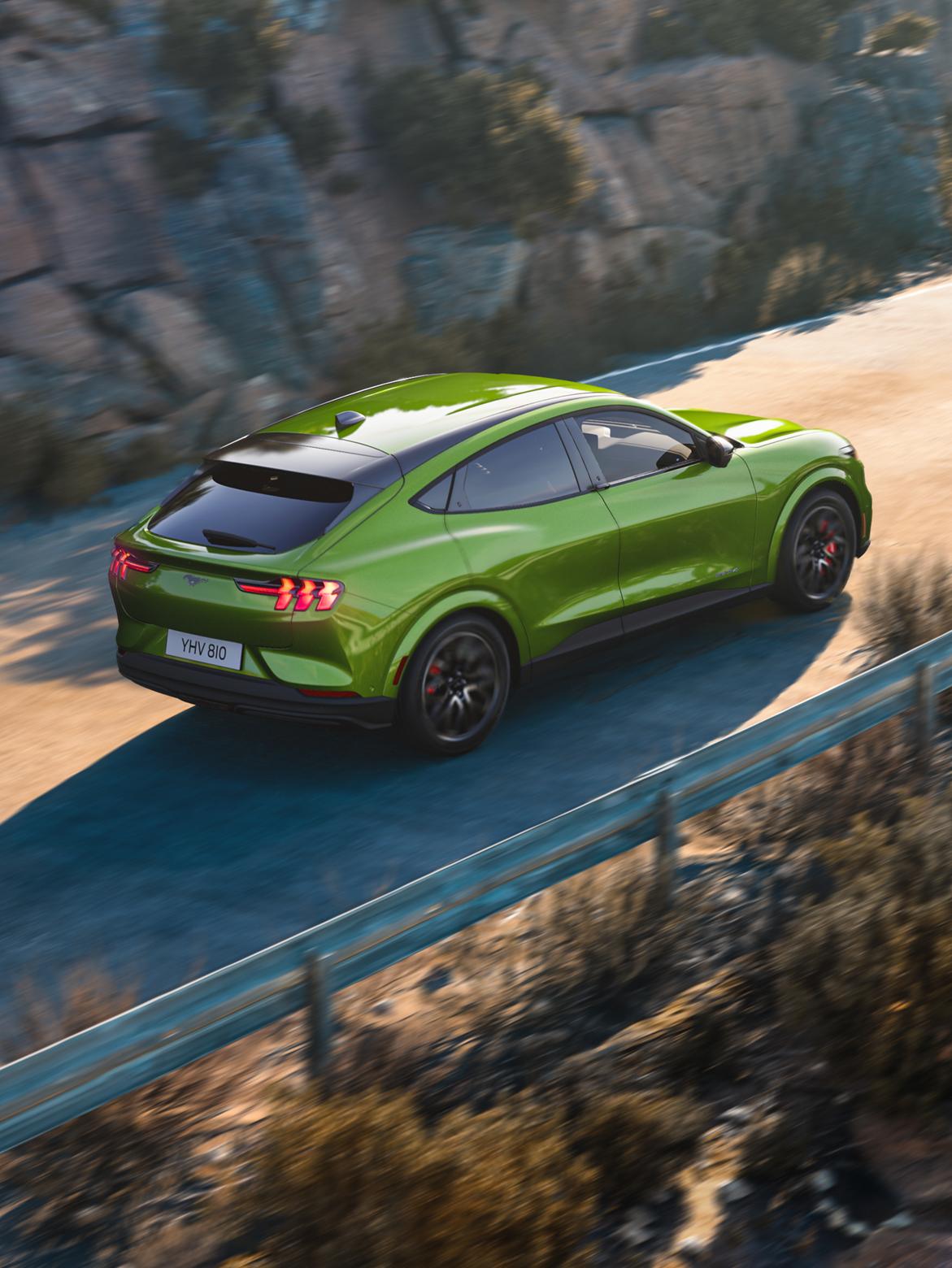 Une Mustang Mach-E verte roulant sur une route de montagne.