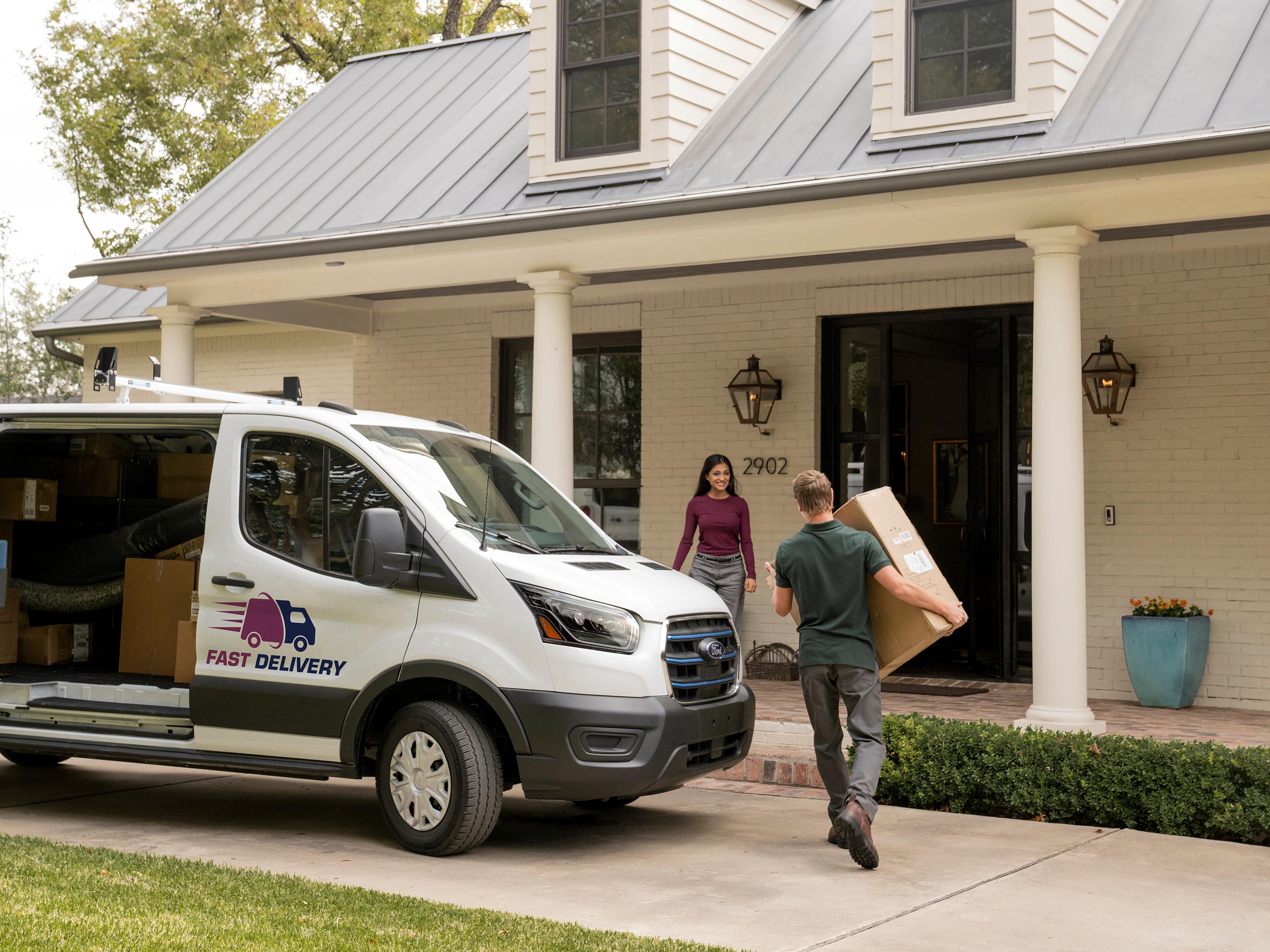 Un homme apportant un colis à une femme devant une maison près d’une fourgonnette Ford Transit® 2027 blanche