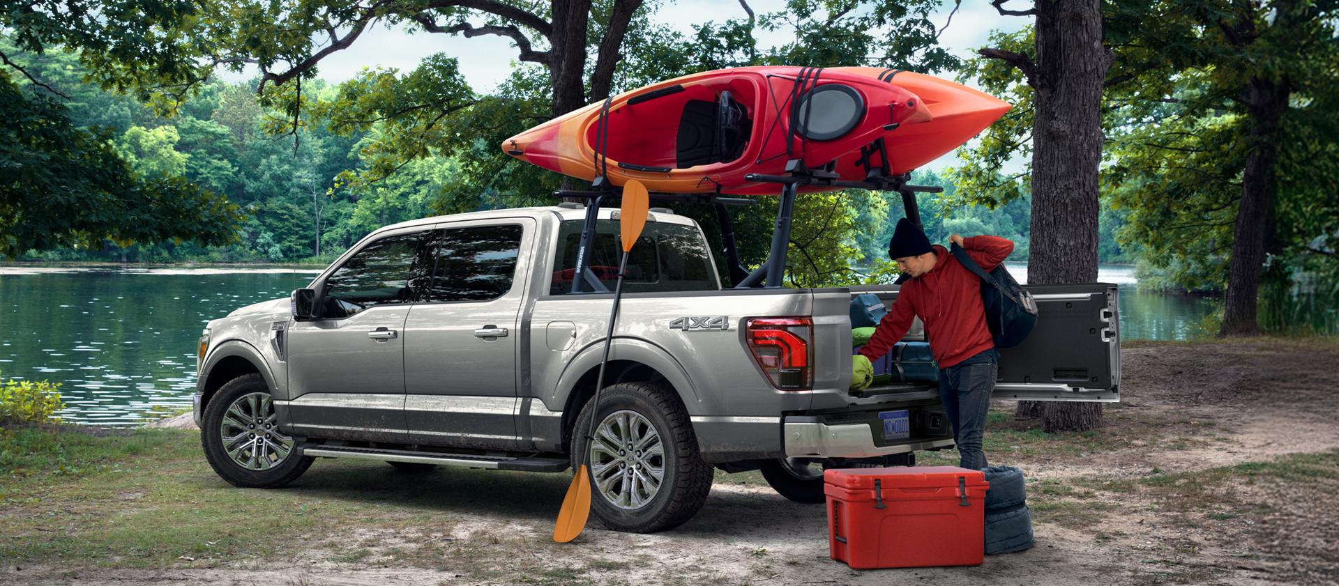 Un F-150 garé près d'un lac, avec un canoë fixé sur le toit, et une personne en train de décharger du matériel de la benne.