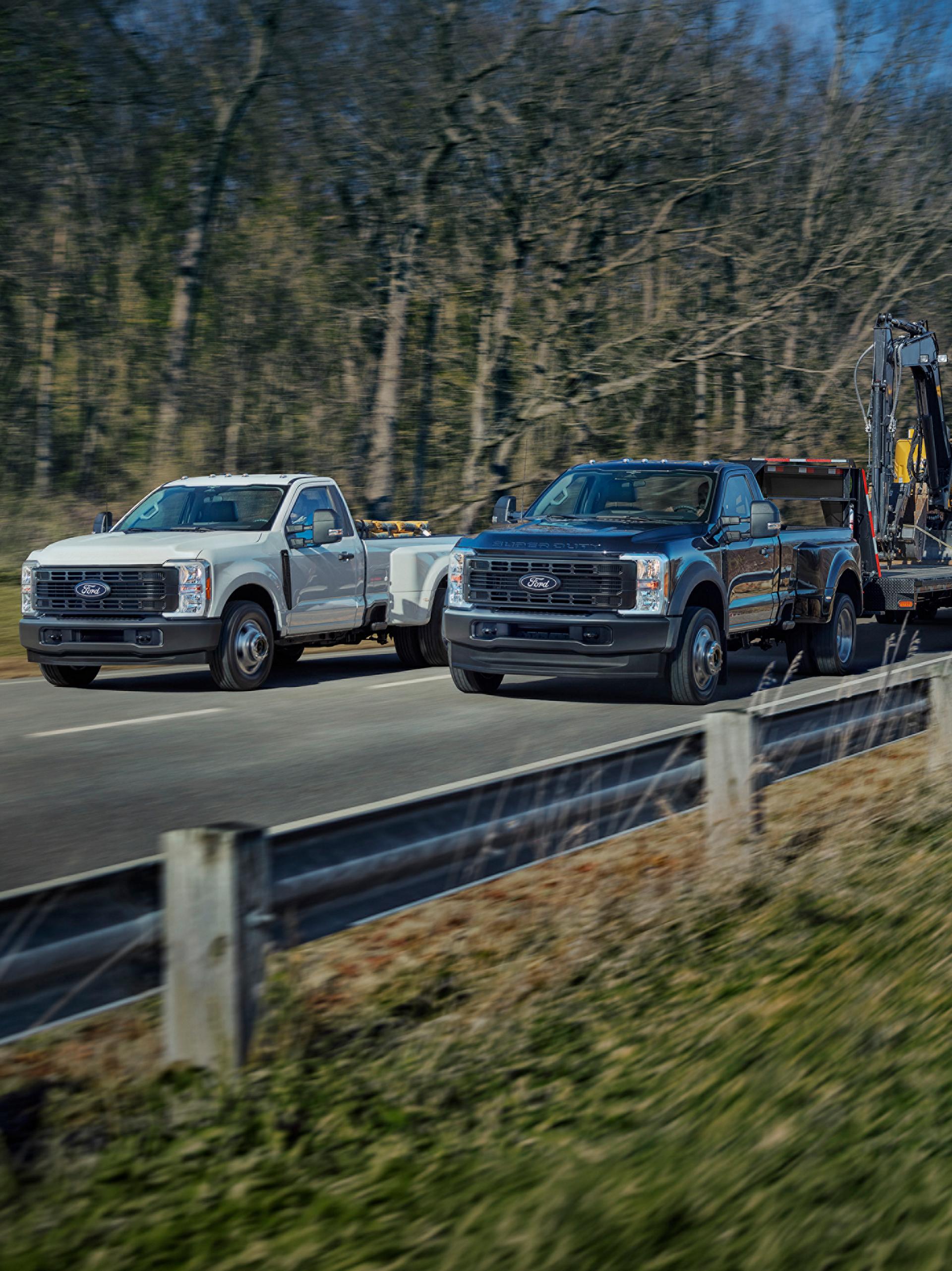 Deux camions Ford Super Duty® 2027 roulant sur une route pavée. L’un transporte des boîtes et l’autre tire une remorque