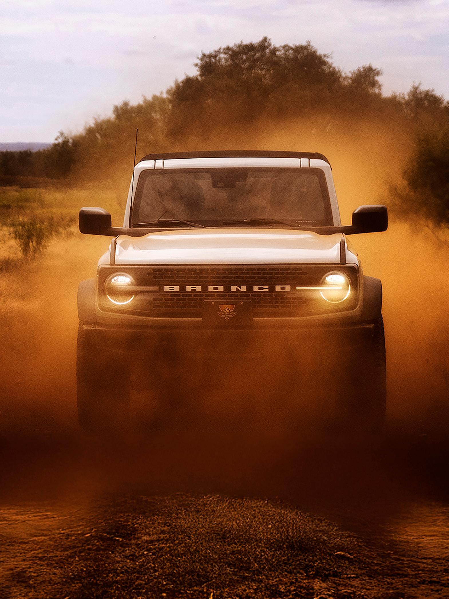 L’avant d’un VUS Ford Bronco® 2026, ses phares brillant à travers un nuage de poussière rouge.