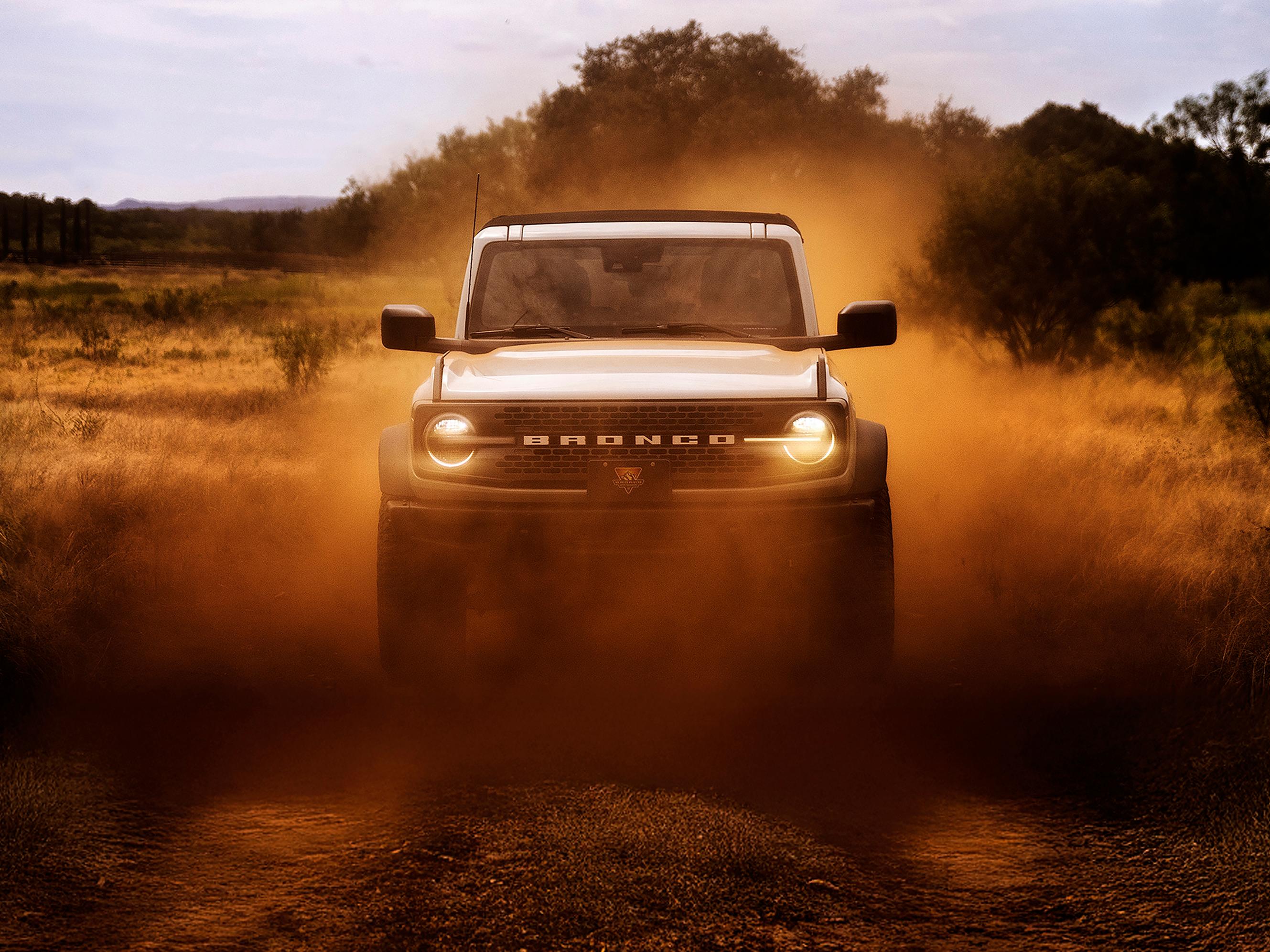 L’avant d’un VUS Ford Bronco®, ses phares brillants à travers un nuage de poussière rouge