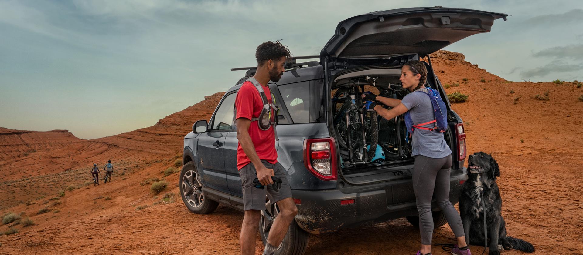 VUS Ford Bronco Sport® 2026 garé dans le désert, avec deux personnes en tenue de randonnée et leur chien à l’extérieur.