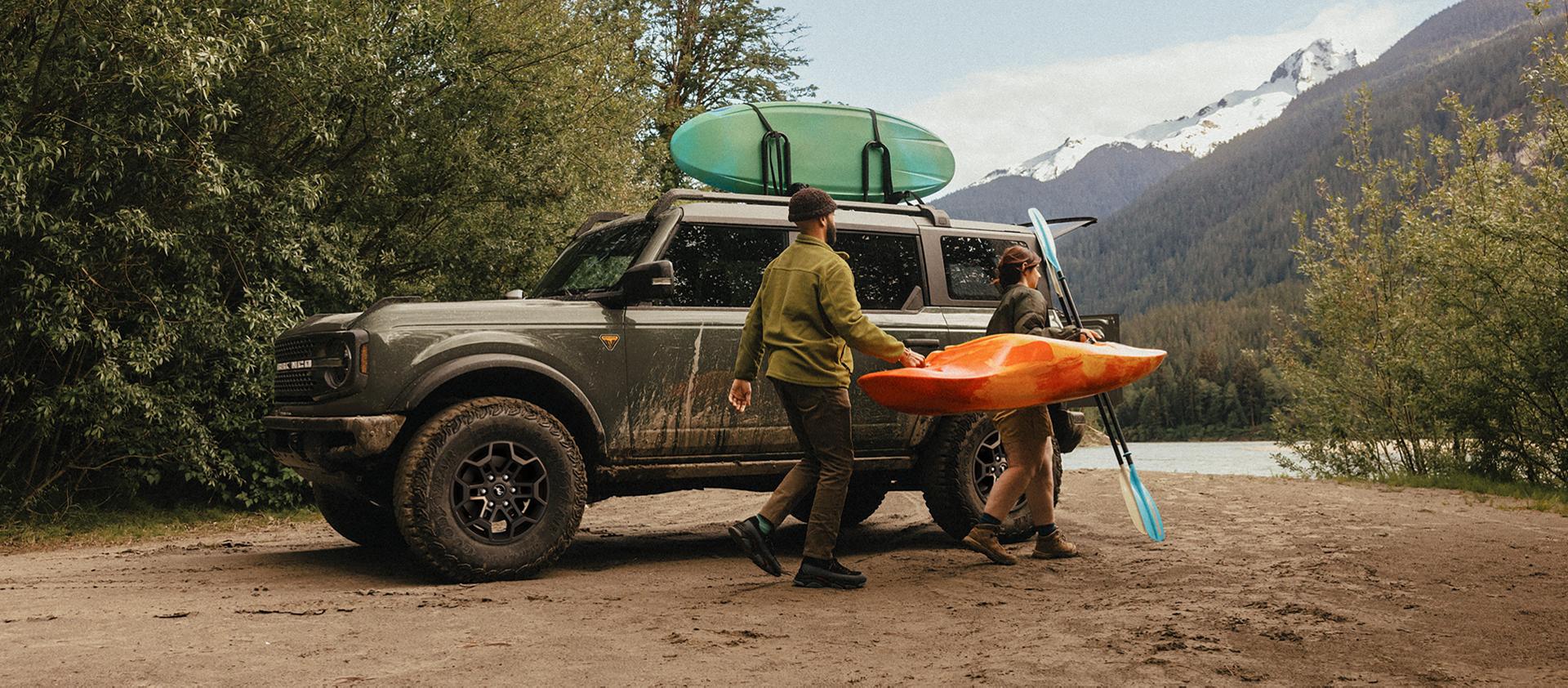 Un homme et une femme transportant un kayak et une pagaie s’éloignent d’un VUS Ford Bronco® 2026 garé sur une vasière
