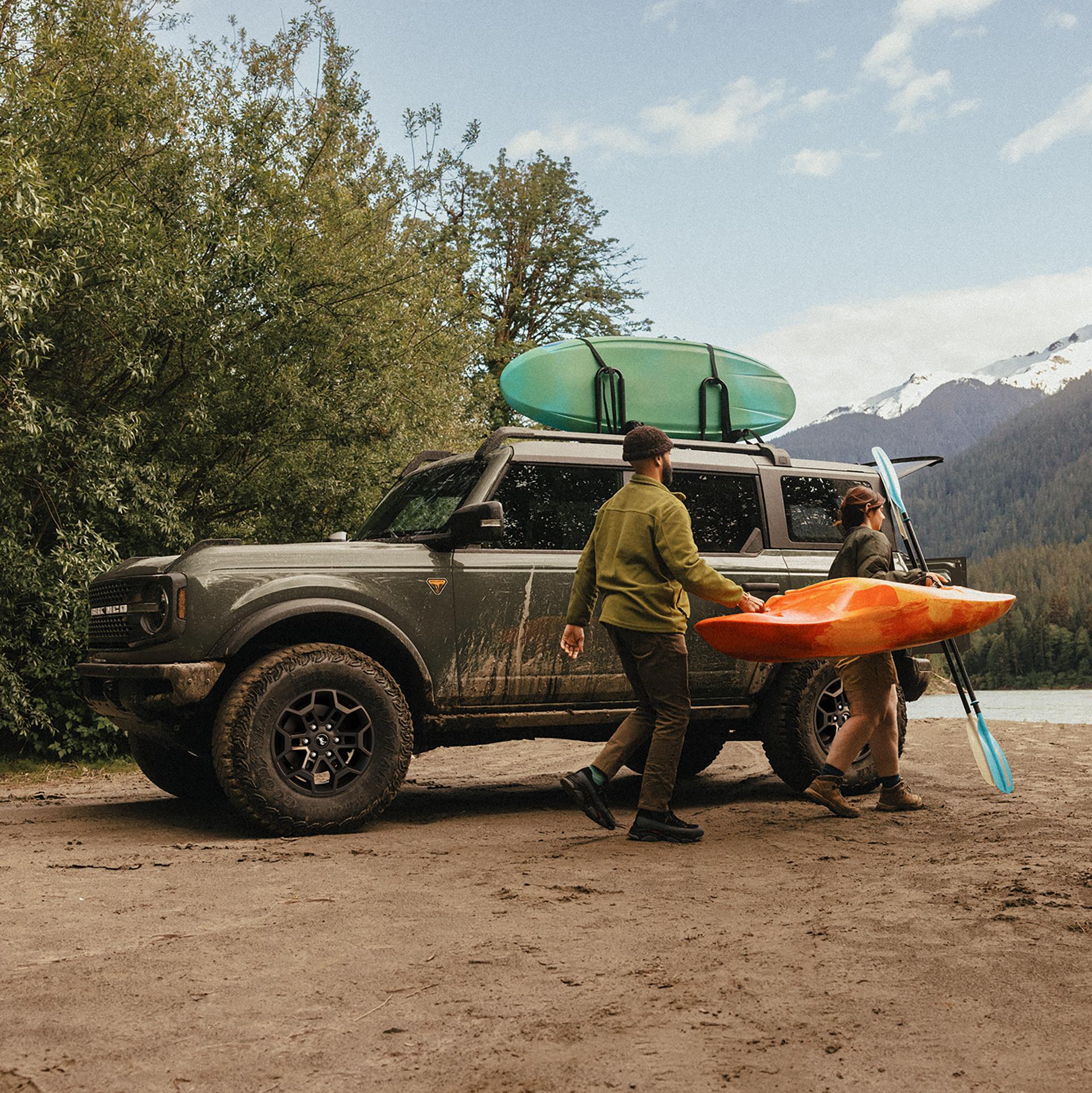Un homme et une femme transportant un kayak et une pagaie s’éloignent d’un VUS Ford Bronco® 2026 garé sur une vasière