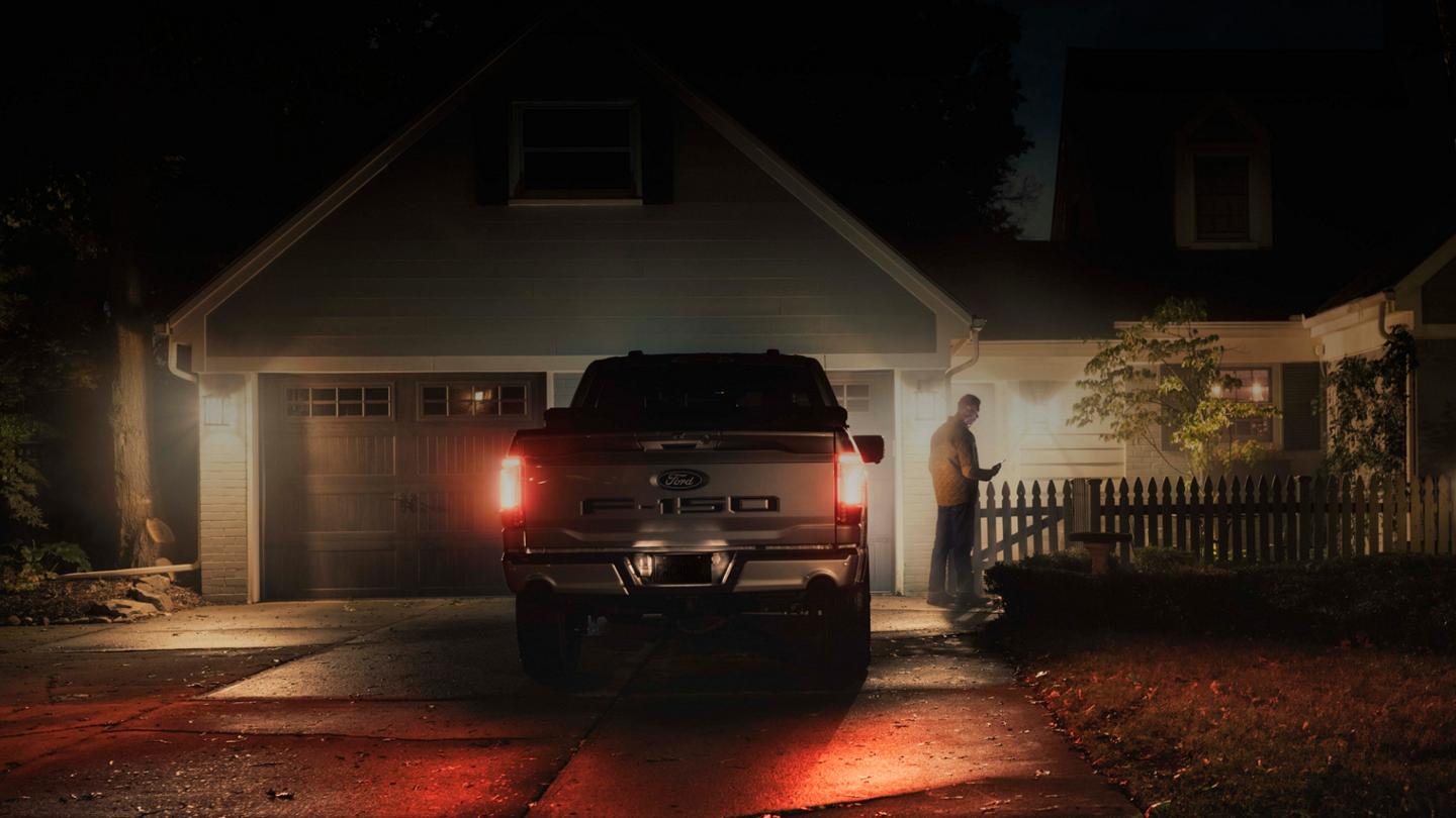 Une personne tenant un téléphone intelligent à côté d’un F-150 Lightning dans une entrée résidentielle.