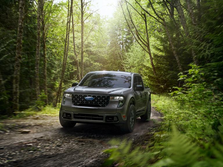 Modèle Ford Maverick® XLT 2026 avec équipement en option montré roulant sur un chemin hors route dans un environnement boisé