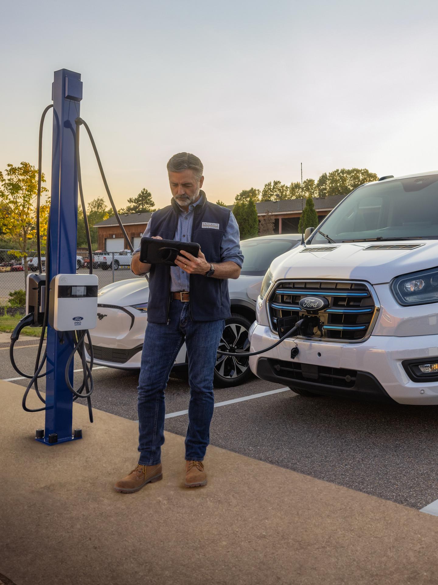 Une personne debout devant une Ford E-Transit stationnée et en cours de recharge.