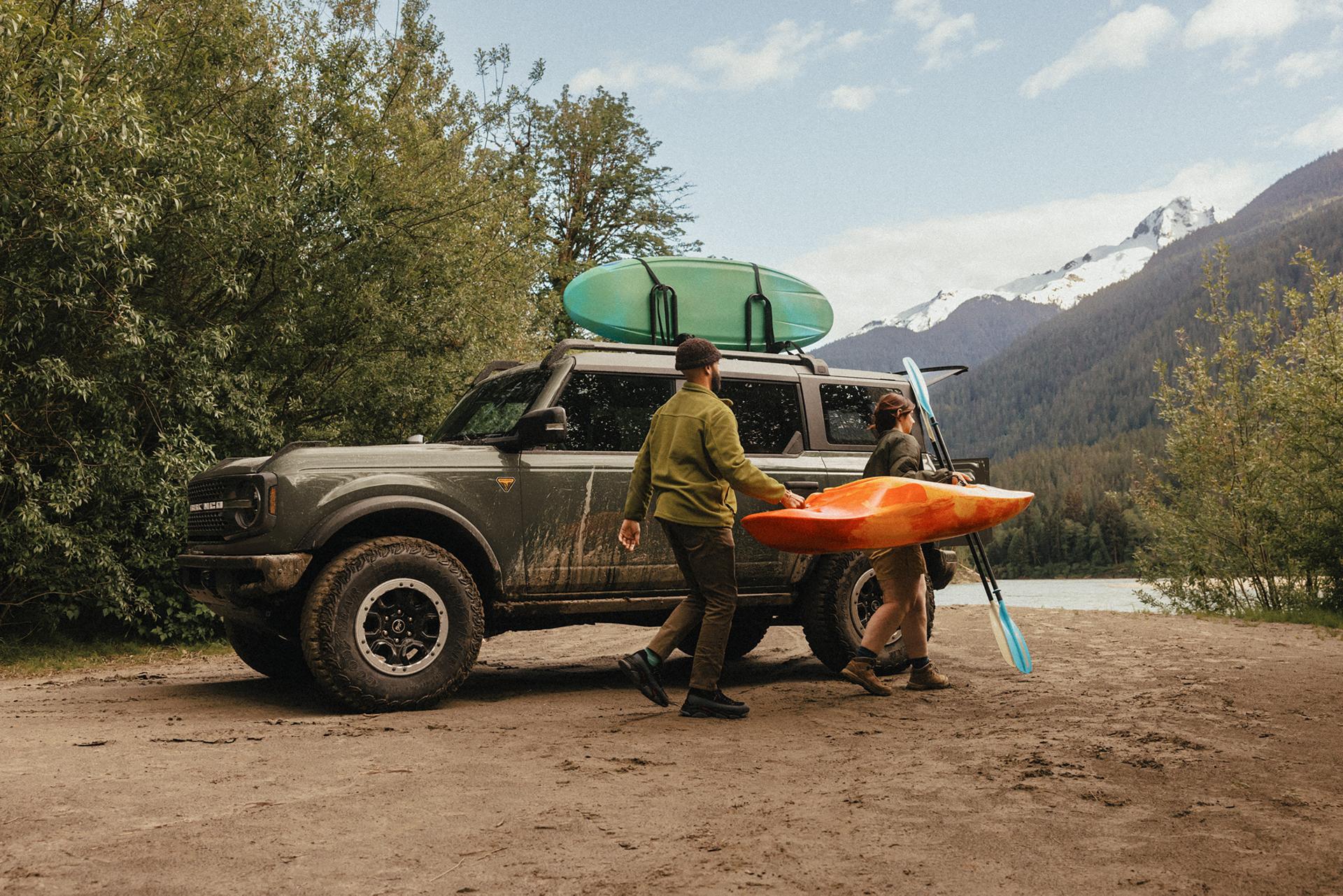 Un homme et une femme s'éloignent, un kayak et une pagaie à la main, d'un VUS Ford Bronco® 2026 garé sur une vasière