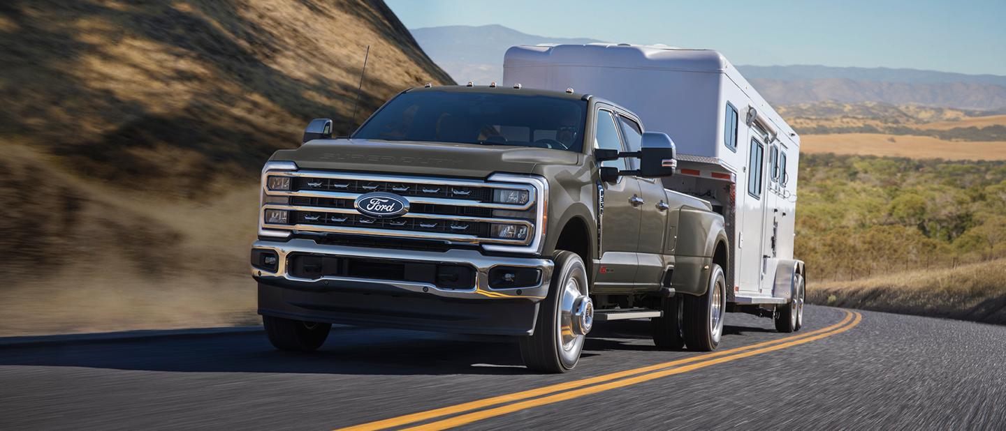 Un camion Ford Super Duty gris tractant une remorque sur une route de montagne sinueuse.