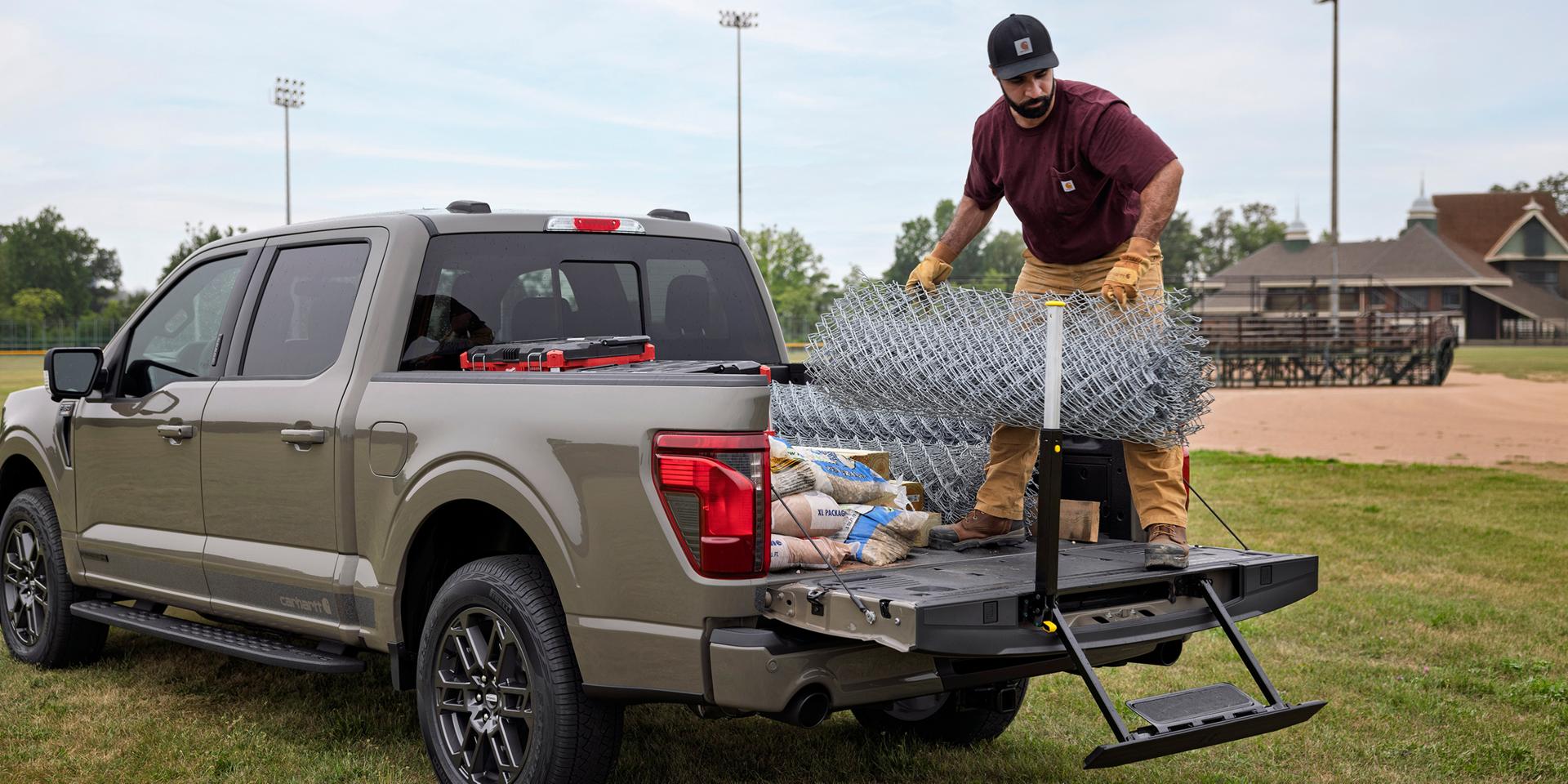 Homme chargeant des panneaux de clôture dans le plateau d’un Ford F-150® XLT 2027 doté de l’ensemble Carhartt®, avec la marche du hayon visible  