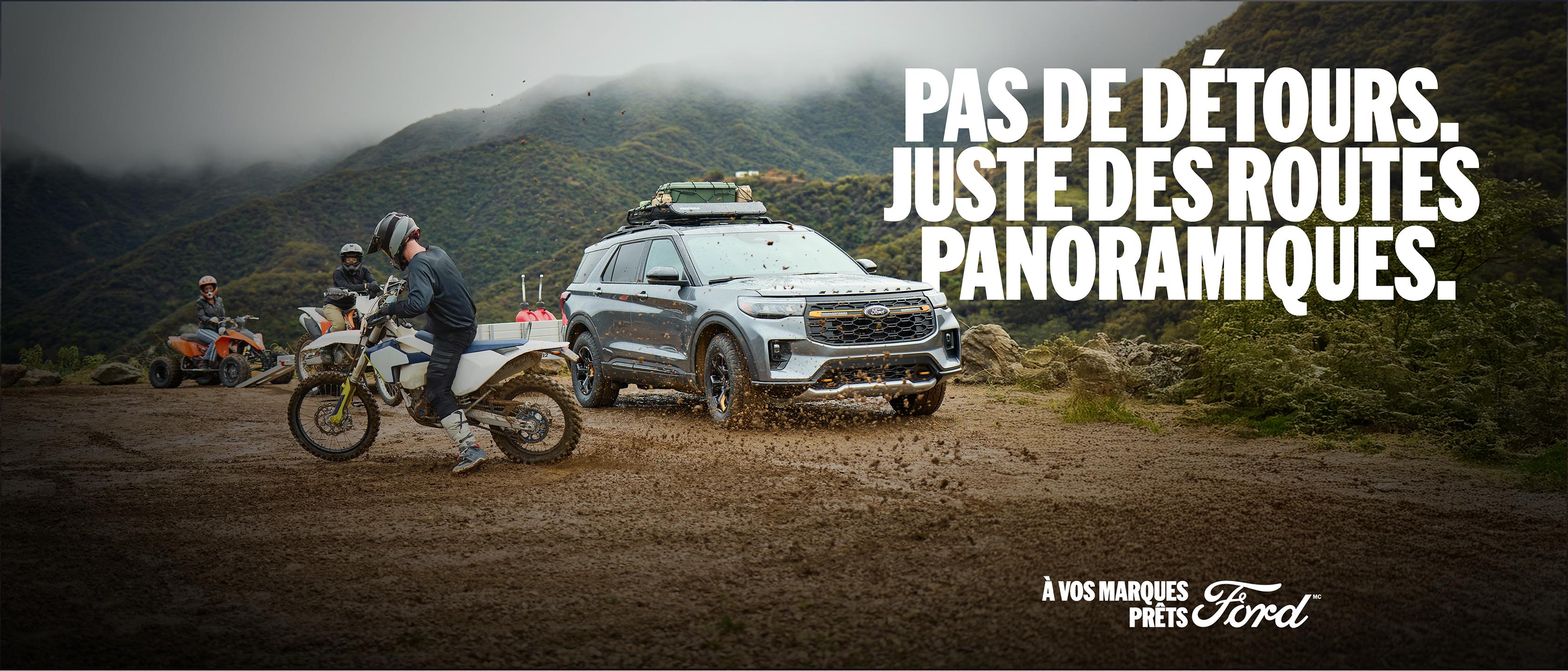 Un Ford Explorer ST 2025 bleu vapeur métallisé circulant sur un chemin de terre sur un terrain vallonné et forestier