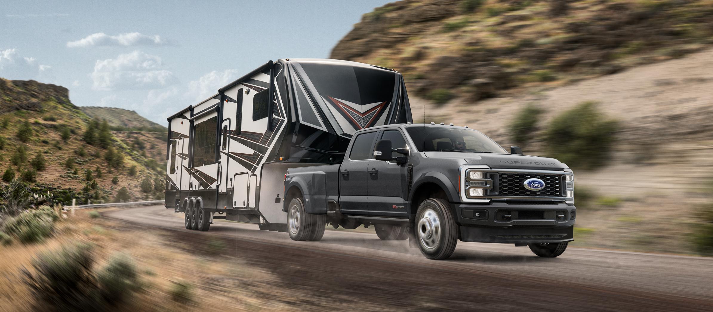 Modèle Super Duty® F-450® Platinum® 2026 en gris carbonisé tirant une caravane sur un chemin de montagne