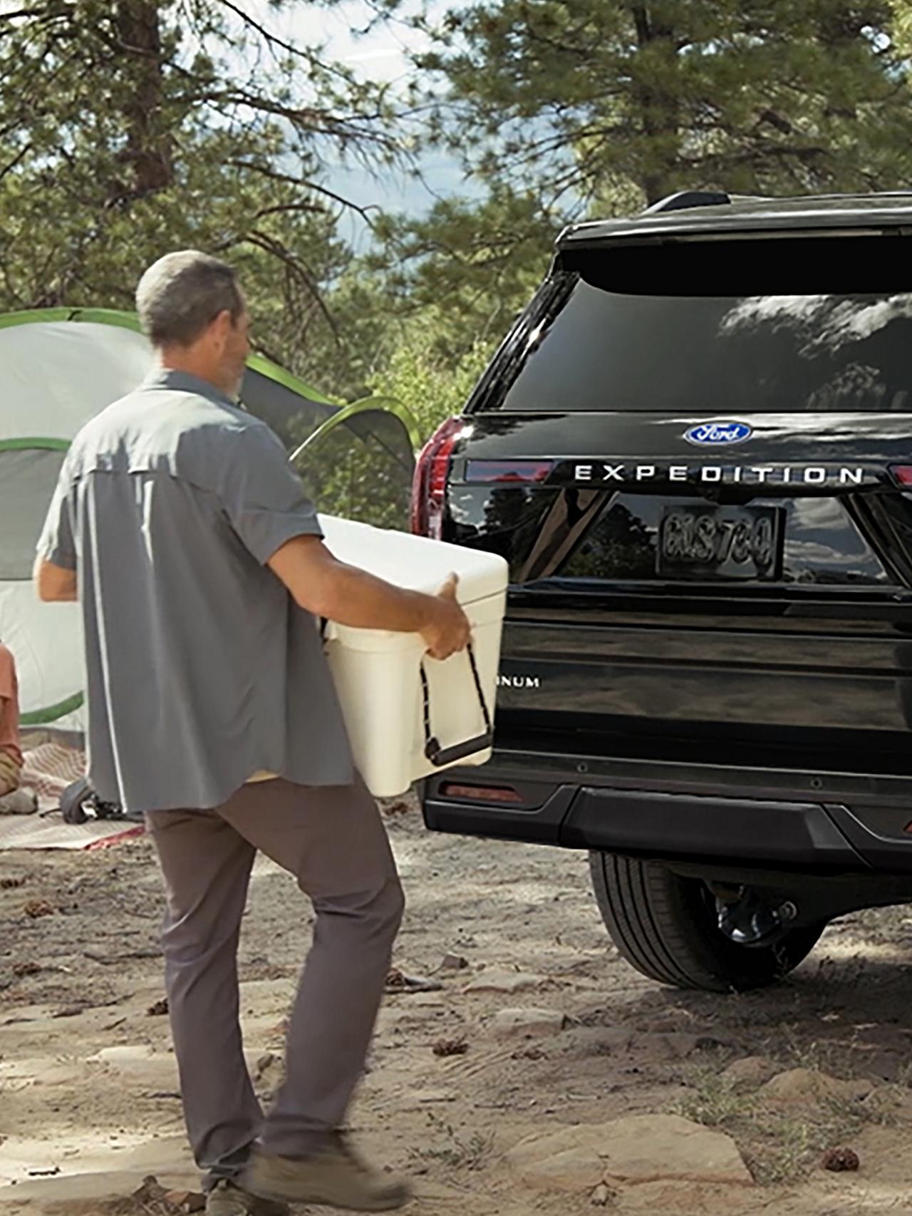 Personne utilisant le portillon divisé Ford avec ouverture à l’approche en option pour charger une glacière dans un VUS Ford Expedition® 2027