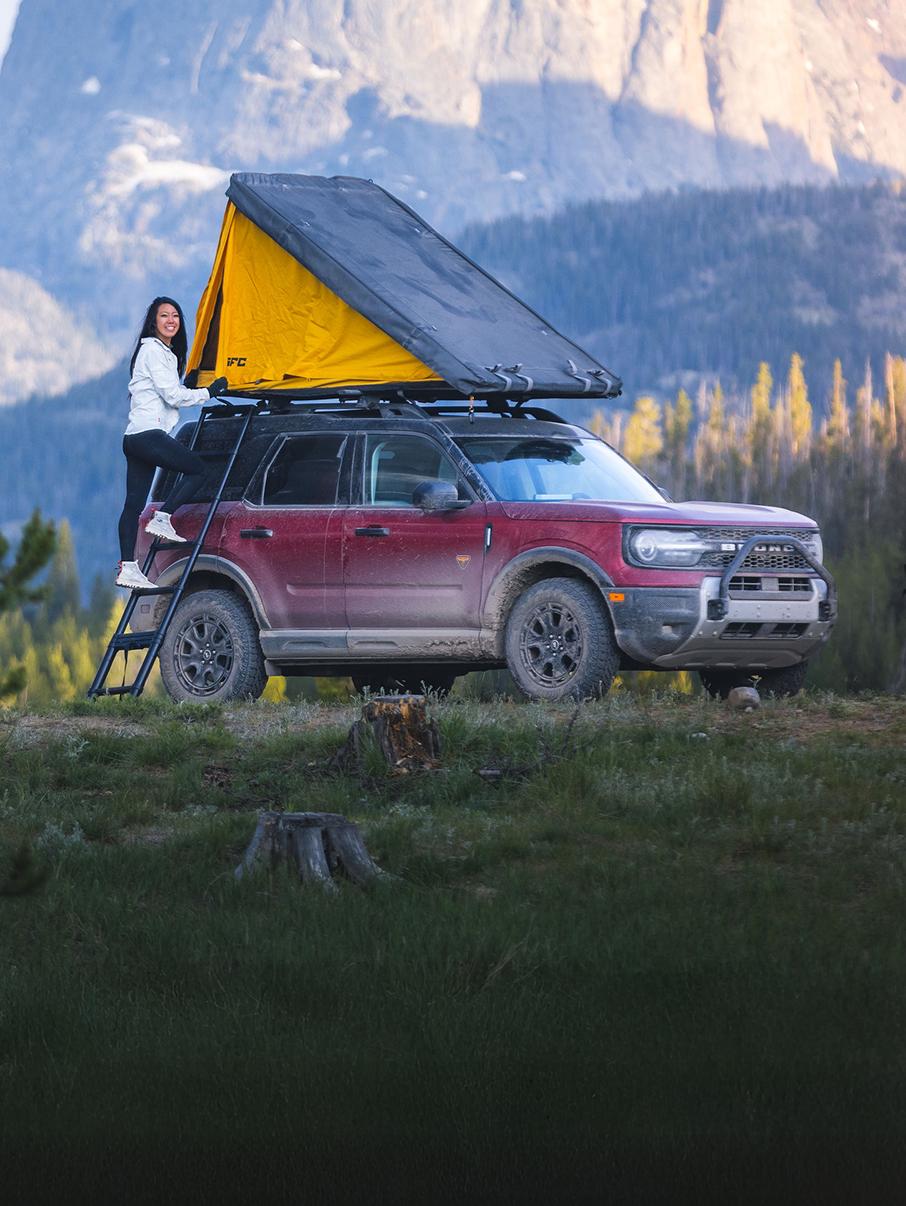 Un Bronco® Sport rouge équipé d'une tente de toit, stationné près d'un terrain de camping.