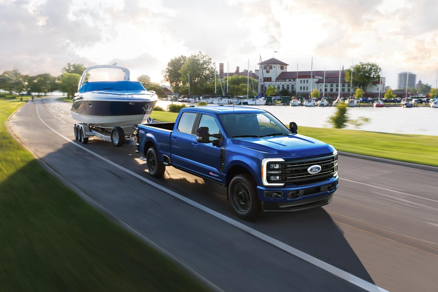 Un modèle Ford Super Duty® F-350® Lariat® 2027 de couleur Bleu Neptune roulant sur une route pavée tout en remorquant un bateau à moteur