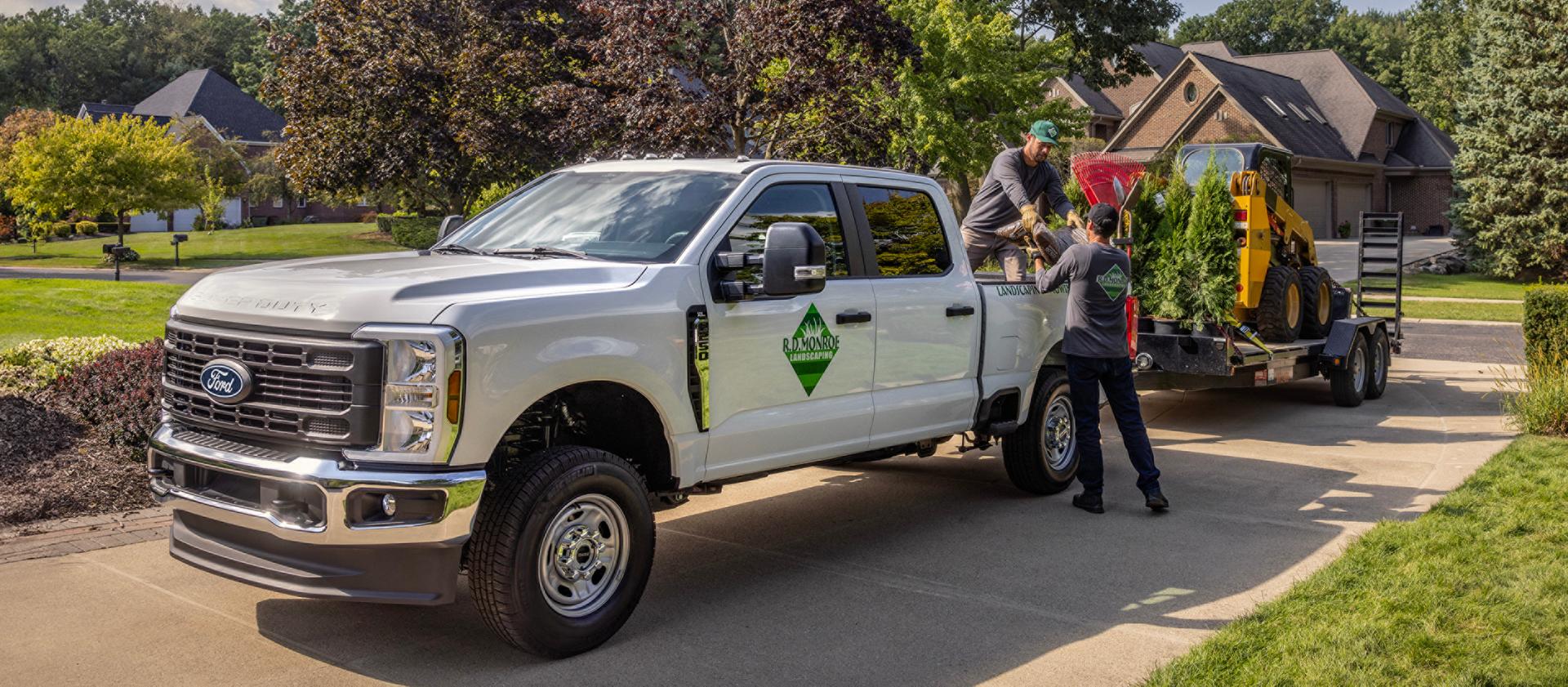 Camion Ford Super Duty® 2027 stationné dans une entrée tirant une grande remorque avec de l’équipement pour l’aménagement paysager